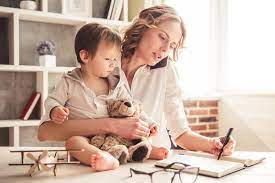 A woman holding a baby and looking at a laptop.